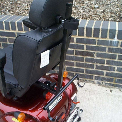 Red mobility scooter with a black adjustable walker holder against a brick wall.