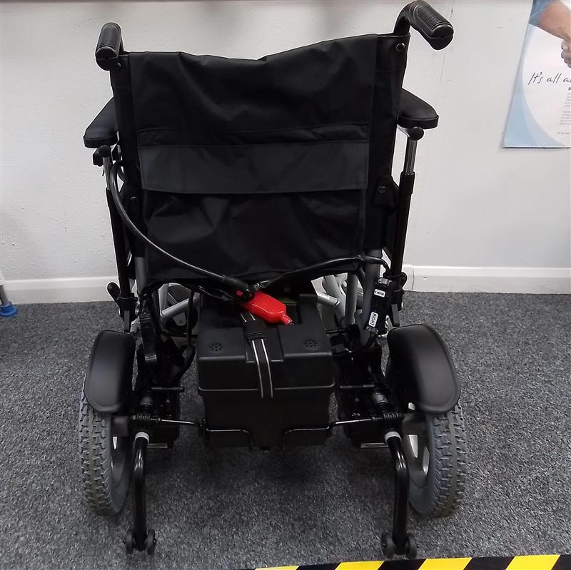 Rear view of black and grey electric powerchair with large wheels and padded armrests on a gray carpeted floor