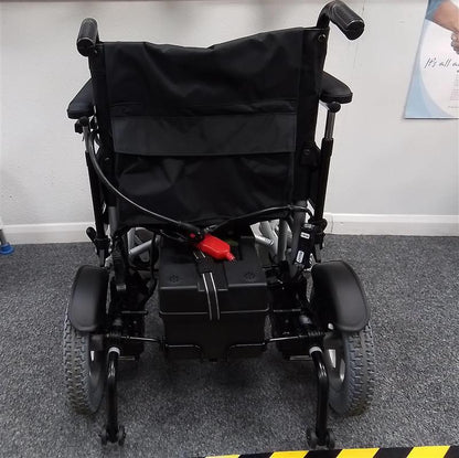 Rear view of black and grey electric powerchair with large wheels and padded armrests on a gray carpeted floor