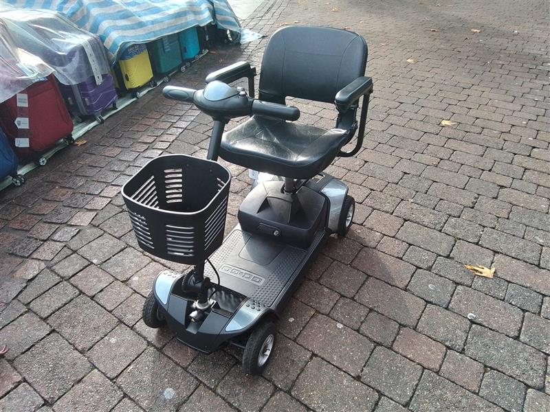 Refurbished Pride Go Go Elite Traveller grey mobility scooter with basket parked on brick pavement outdoors