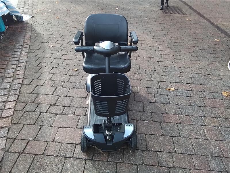 Refurbished Pride Go Go Elite Traveller mobility scooter in grey with basket on front, shown on paved outdoor surface